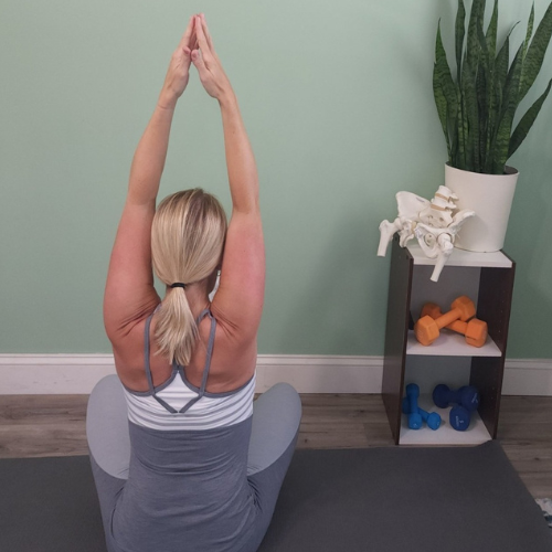 A woman sitting with her back to the camera has her hands above her head touching